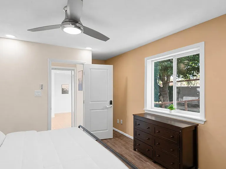 Bedroom with ceiling fan, large window, and dresser storage, plus easy access to the hallway.