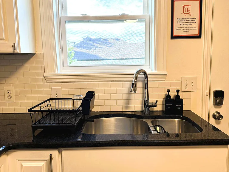 Kitchen sink station with dark counters, white cabinetry, and a window above the sink for natural light and ventilation.