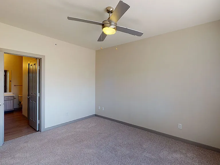 Spacious apartment bedroom with attached bathroom and plush carpet flooring.