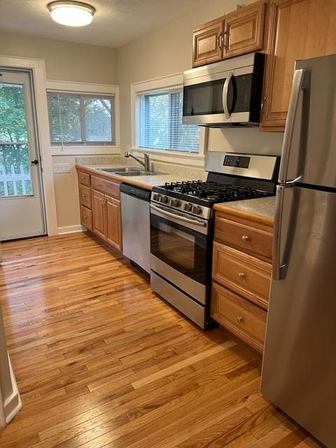 Kitchen with hardwood floor, new cabinets and new stainless steel appliances including a dishwasher. Small balcony outside kitchen door.