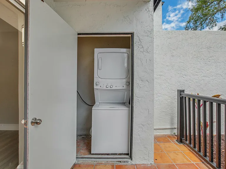 Convenient in-unit laundry area featuring a sleek stacked washer and dryer, set against a charming outdoor entry with terracotta tiles.