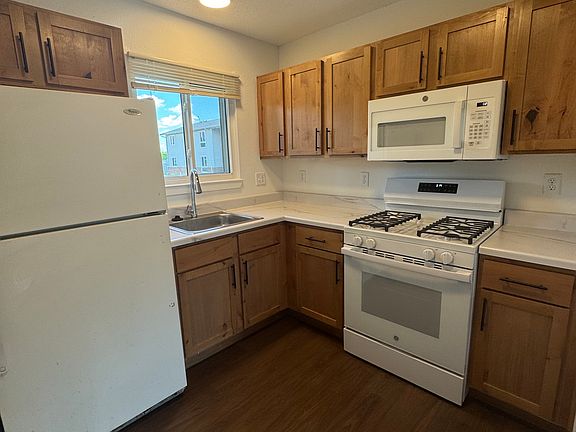 Charming modern kitchen with refrigerator, gas stove and overhead microwave, natural wood cabinetry, and elegant marble-look countertops.