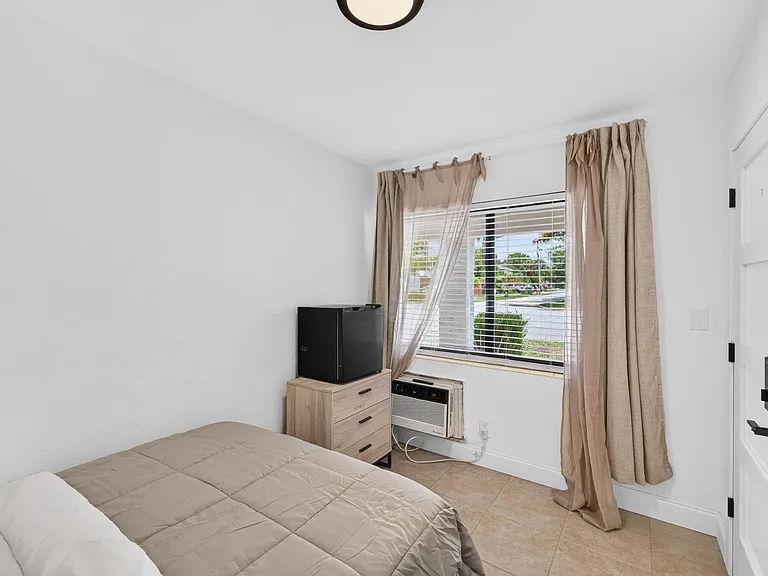 Private bedroom with a large window, neutral finishes, and space for a bed and small dresser, plus in-room A/C.
