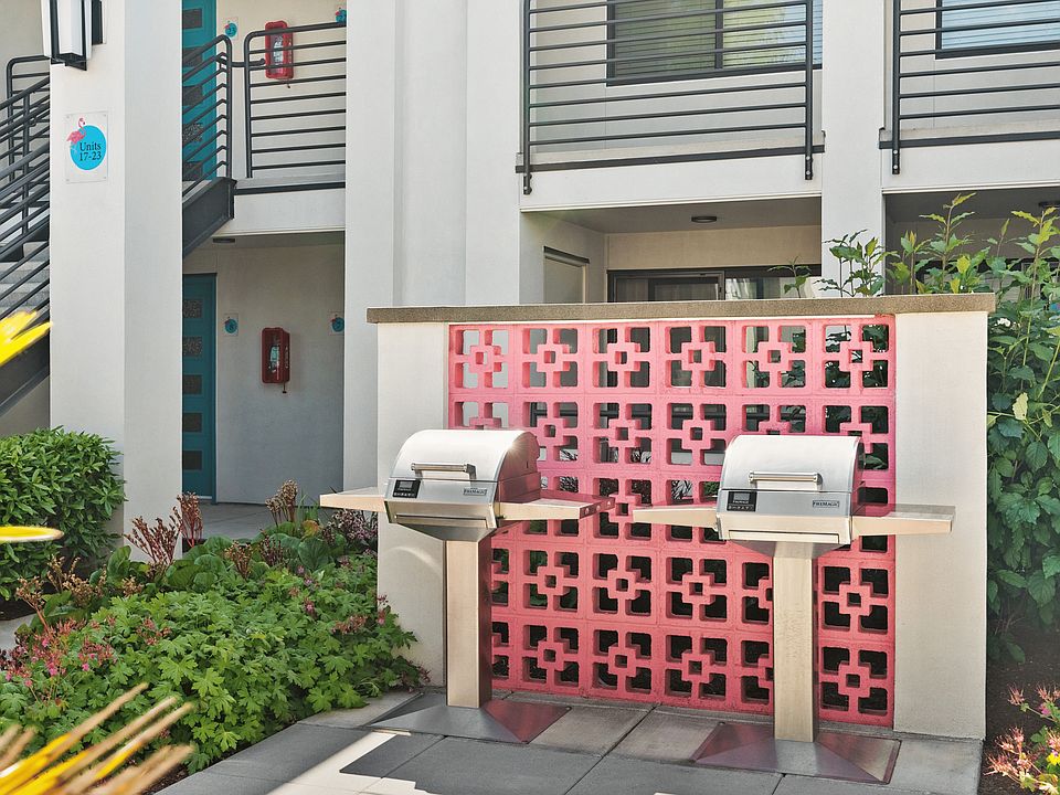 Charming apartment complex with stylish outdoor BBQ area, accented by a vibrant pink decorative wall and lush greenery.