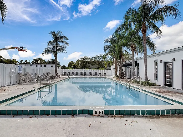 Inviting outdoor pool area with palm trees, comfortable lounge chairs, and a vibrant blue sky backdrop.