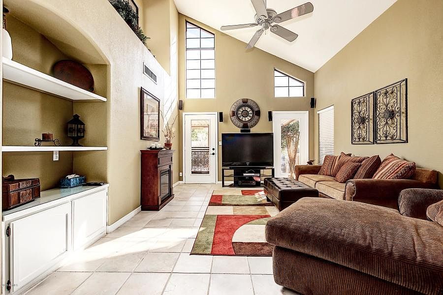 Living room with vaulted ceilings, wall shelving. Tile throughout.