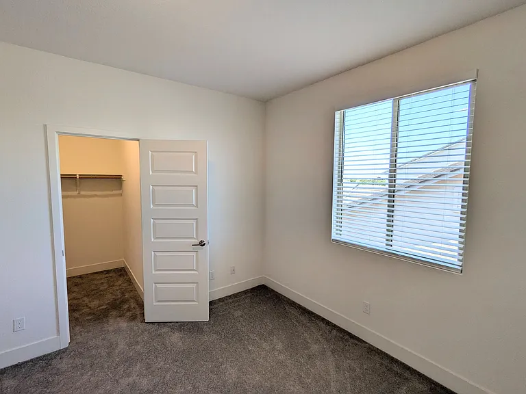 This comfortable secondary bedroom offers a bright, inviting atmosphere. It features a spacious walk-in closet and large windows with custom horizontal blinds, providing the perfect balance of privacy and natural light.