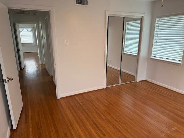 Spacious room featuring wood-finish flooring, white walls, and a mirrored closet door