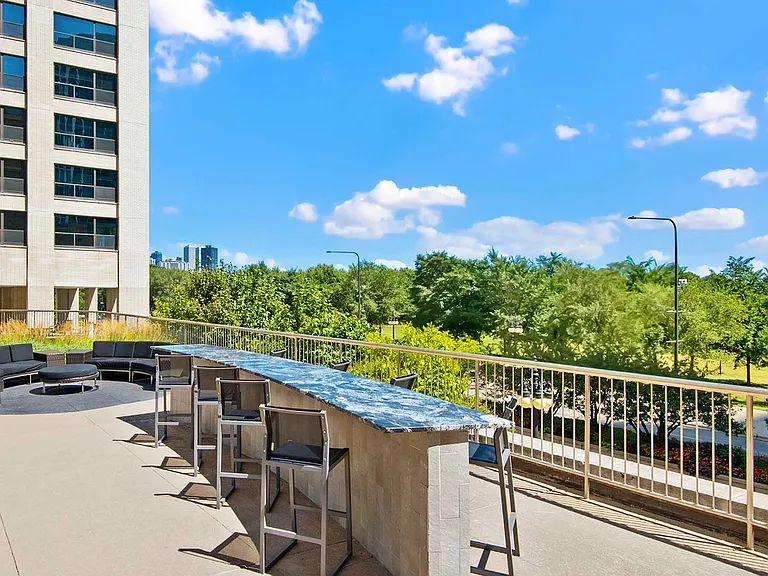 A bar sits along the railing of the sundeck with more seating behind it and the Eleven Thirty tower rising behind further. Grant Park and the Chicago skyline can see see in the distance.
