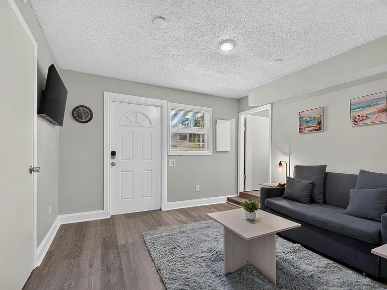 Living room with durable flooring, wall-mounted TV, and seating area anchored by a coffee table near the entry.