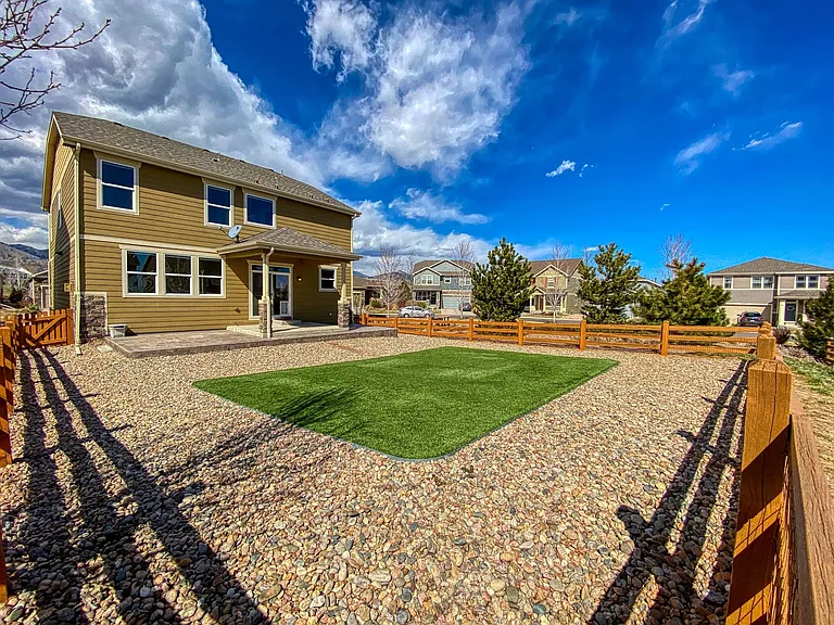 No-maintenance fenced-in backyard with realistic artificial grass, river rock, covered patio, natural gas line for grill, and views of North Table Mountain.