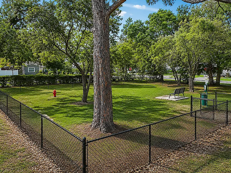 Charming fenced green space with lush trees and a welcoming bench, perfect for your pup to play!