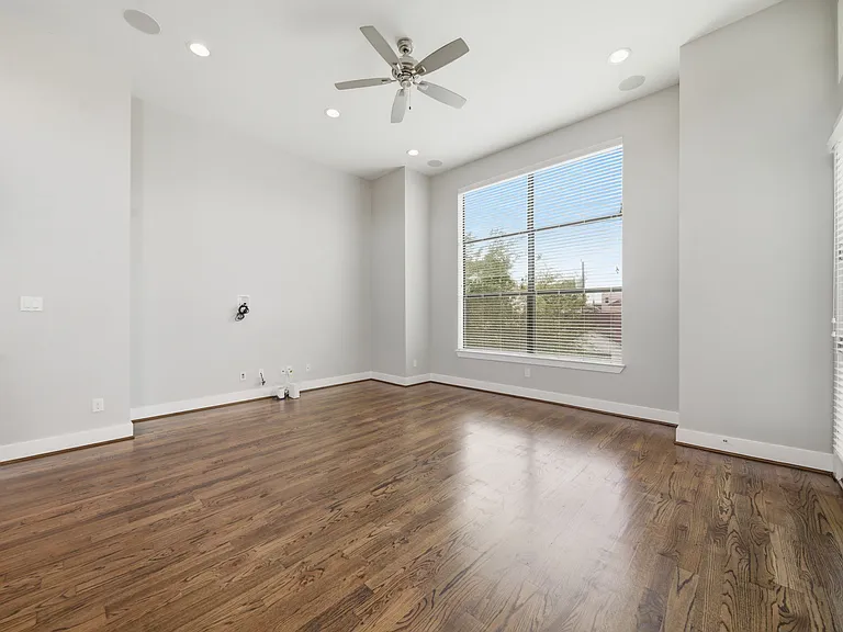 Bright and spacious living area featuring rich hardwood floors, expansive windows that flood the space with natural light, and a seamless flow into the open-concept kitchen. Thoughtful details like recessed lighting and a ceiling fan.