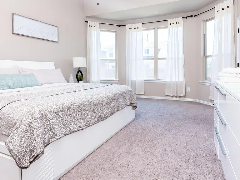 Spacious bedroom with a large window bay, neutral finishes, and room for a dresser or desk alongside the bed.