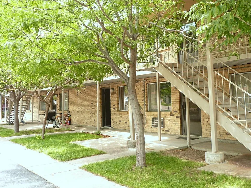 Inviting apartment exterior with brick facade, lush greenery, and a staircase leading to upper units.