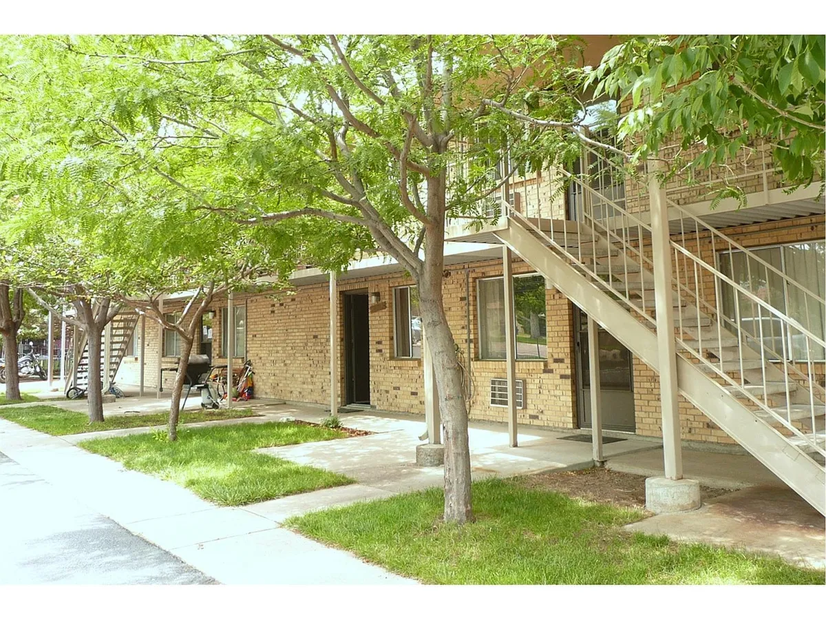 Inviting apartment exterior with brick facade, lush greenery, and a staircase leading to upper units. - 10705 W 7th Ave
