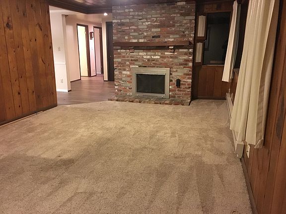 Living room with wood-burning fireplace, looking past the dining room on left, down the hall past the entry door to the main bathroom and two main floor bedrooms, as well as the hall to the family room.