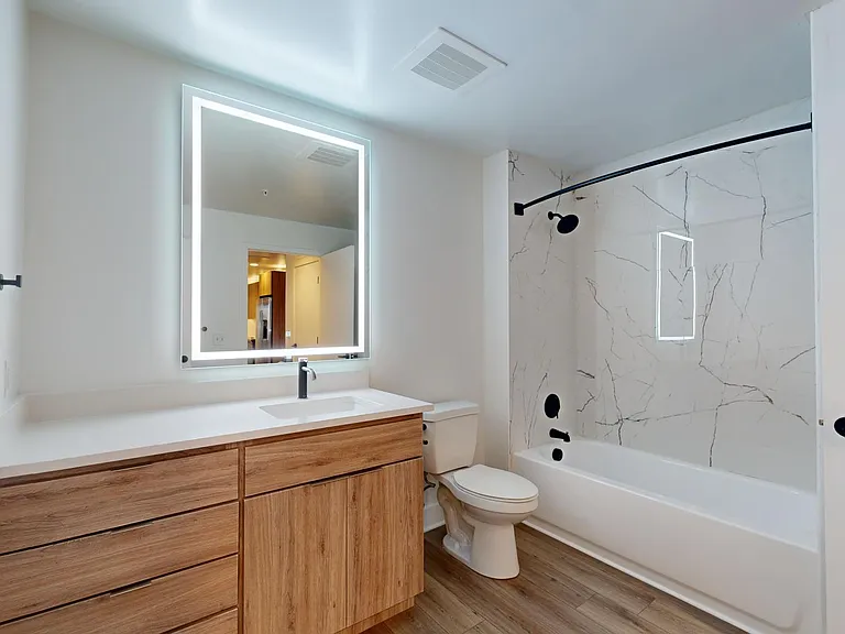 Apartment bathroom with wood-style flooring and LED vanity mirror.