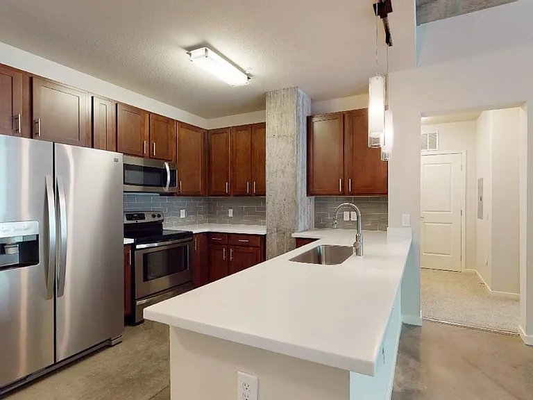 Apartment kitchen with stainless steel appliances, quartz countertops and polished concrete flooring.