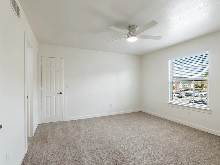 Bright, cozy bedroom with plush carpet, white walls, and a large window for natural light. Bright, cozy bedroom with plush carpet, white walls, and a large window for natural light.