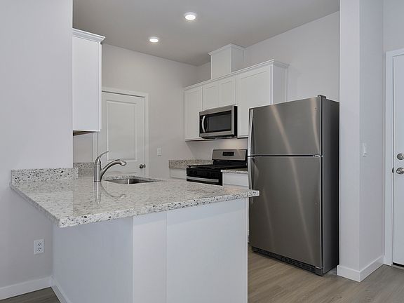 The kitchen has stainless steel appliances and plank flooring.