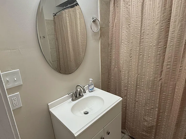 Full bathroom with a vanity sink, wall mirror, and overhead lighting, plus a tub/shower with curtain and tiled surround.