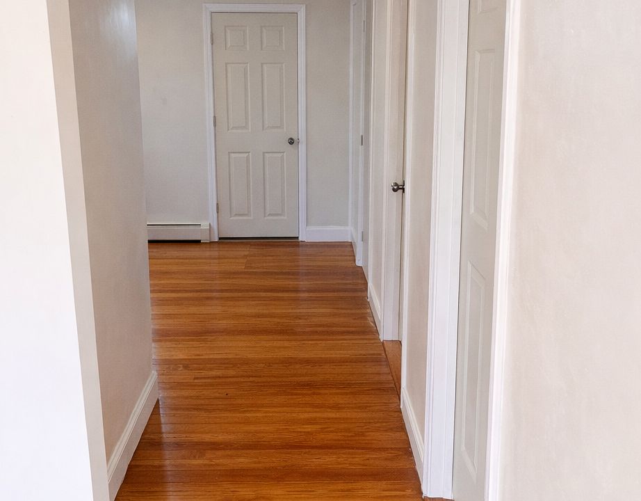 Hallway from living area leading to dining/ kitchen, & doors to bathroom, storage closet, and 3 bedrooms.