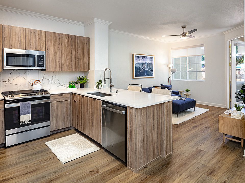 Apartment kitchen with stainless steel appliances, dining and living room with wood-style flooring.