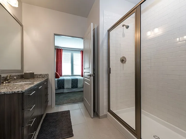 Bath with granite countertops, brown cabinetry, hard surface flooring and tiled shower