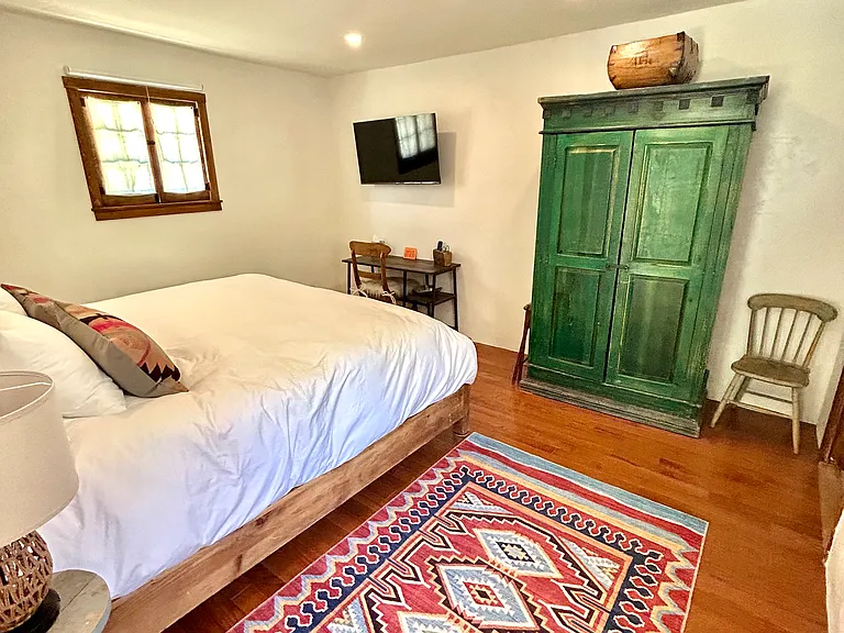 Antique armoire with clothes hangers, mirror and shelves, smart tv and work area in casita bedroom