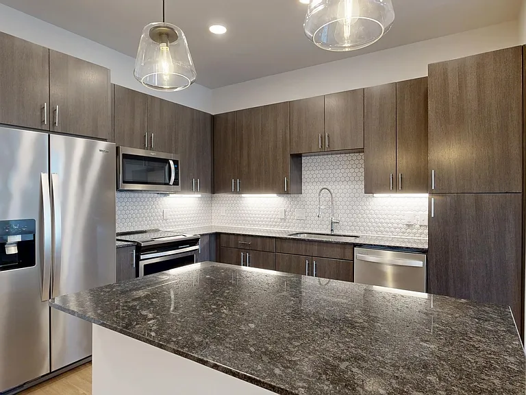 Apartment kitchen with stainless steel appliances, granite countertops, and wood-style flooring.
