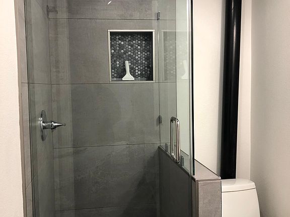 Glassed enclosed shower with penny round blue mosaic tile floor and niche.