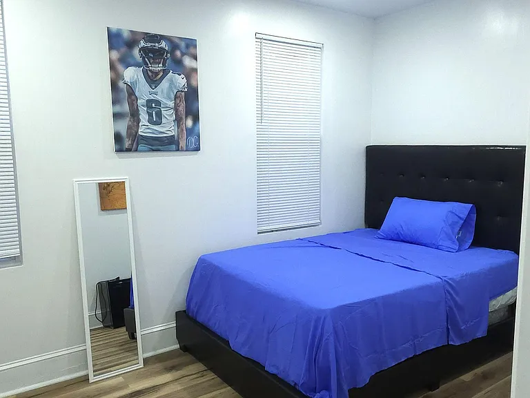 Furnished bedroom with a full-size bed, wood-look flooring, and two windows with blinds for light and privacy.
