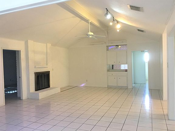 The vaulted ceiling living room with a fireplace, ceiling fan, access lighting, and more