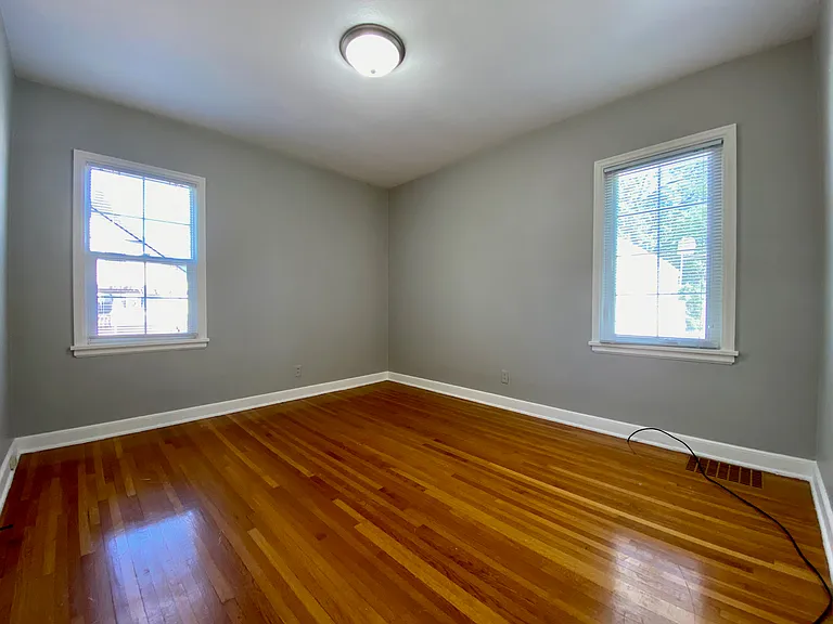Bright and inviting room with polished hardwood floors, two large windows, and a central ceiling light, perfect for a cozy bedroom or home office. Bright and inviting room with polished hardwood floors, two large windows, and a central ceiling light, perf