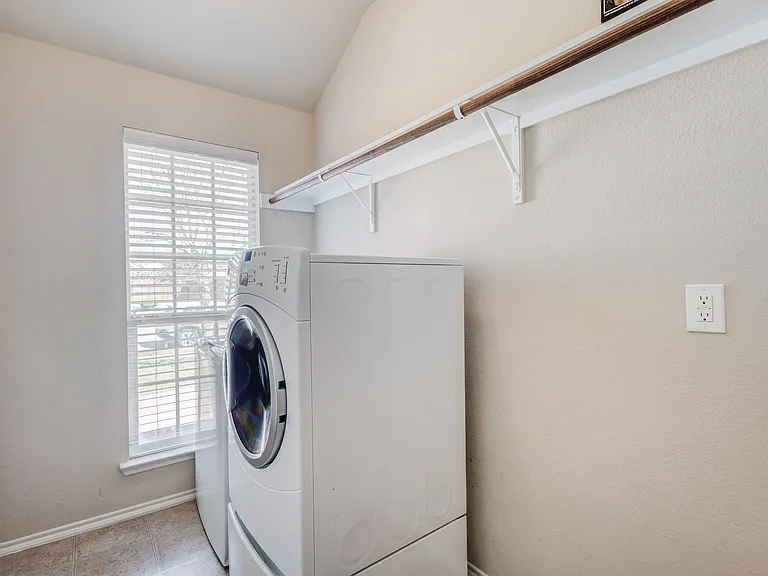 View of the laundry room showing a storage shelf and hanging rod for clean laundry- notice the window an dhow it brightens this area