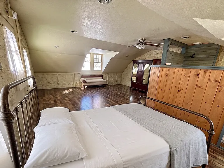 Expansive upper primary suite featuring unique stone architecture, a king bed, daybed, ample clothing storage, and a private balcony.