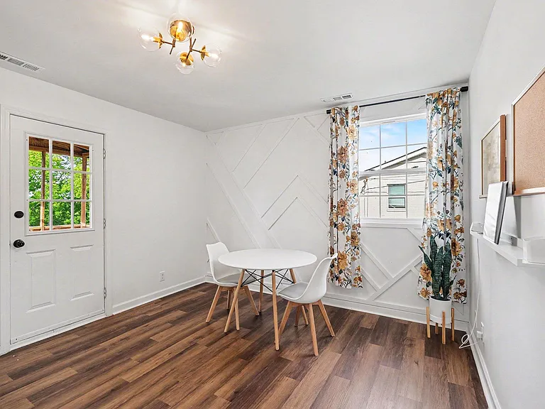 Dining nook with a round table, stylish lighting, and easy access to an exterior door and large window with curtains.