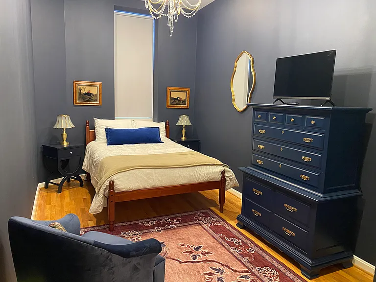 Bedroom #2, the blue room, with double bed, chest, smart TV, armchair, and ensuite bath