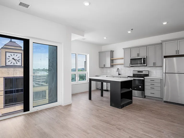 Modern open-concept kitchen with sleek gray cabinets, stainless steel appliances, and wood flooring, featuring a picturesque window view of a clock tower. Modern open-concept kitchen with sleek gray cabinets, stainless steel appliances, and wood flooring,