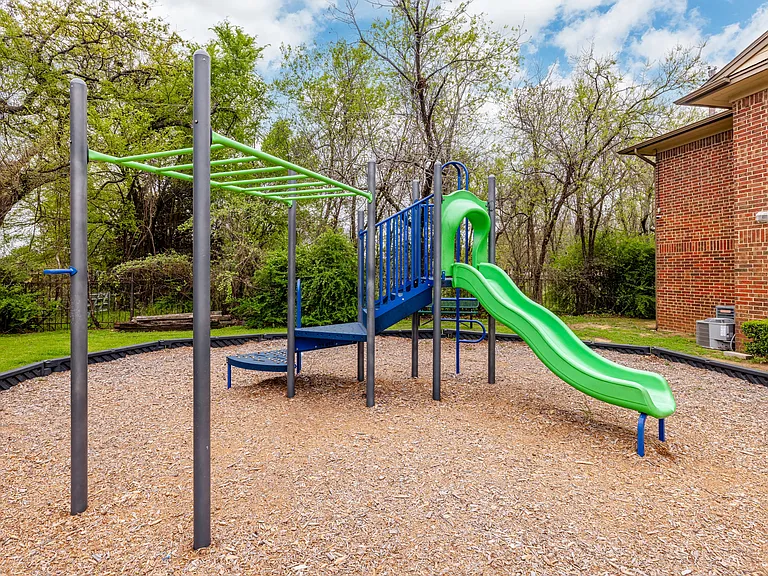 Playground swings and slide set surrounded by shaded trees