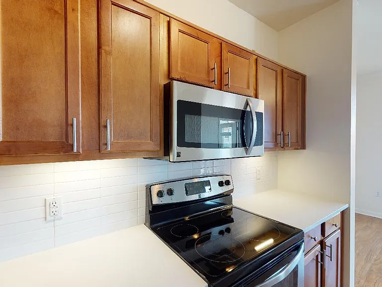 Apartment kitchen with stainless steel appliances and wood-style flooring. Quartz-style countertops (shown here) are available in select homes.