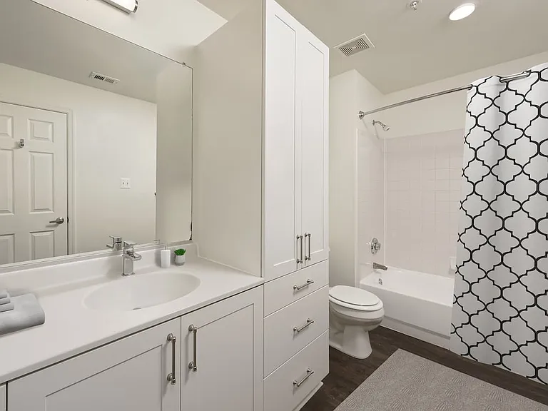 Renovated Package II bath with white cultured marble countertops, white cabinetry, and hard surface flooring