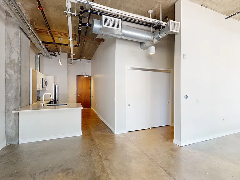 Apartment kitchen with stainless steel appliances, dining and living room with concrete or wood-style flooring.