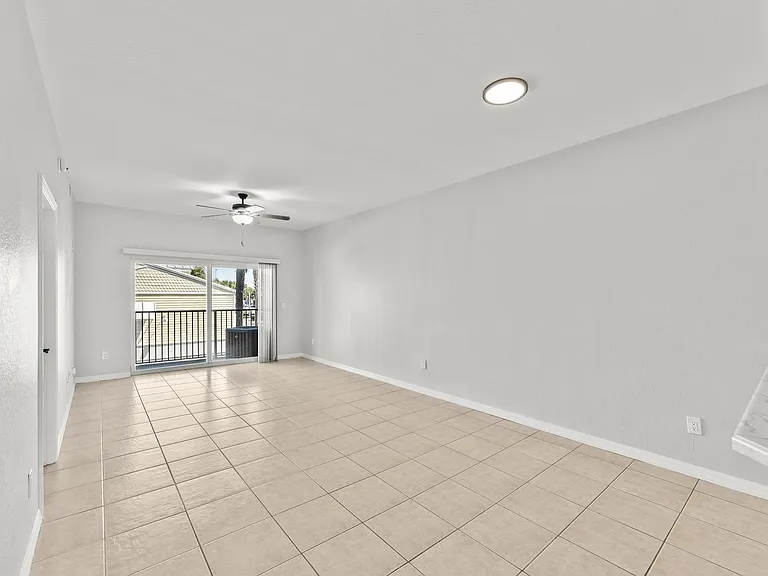 Bright open-plan living area with elegant tile flooring, modern ceiling fan, and expansive sliding doors leading to a sunlit balcony.