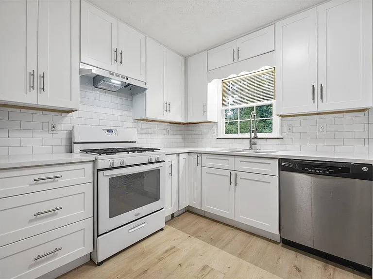 U-shaped kitchen with shaker cabinetry, subway-tile backsplash, gas range, dishwasher, and a window over the sink.