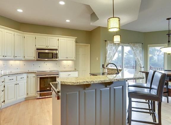 Kitchen with a centrally located center island that boasts a seating counter. Designer kitchen with white cabinets, two different granite countertops and new light fixtures.  This blending of color & materials is gorgeous!