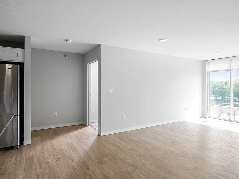 Bright and open apartment living area with sleek hardwood floors, stainless steel appliances, and expansive windows overlooking greenery. Bright and open apartment living area with sleek hardwood floors, stainless steel appliances, and expansive windows o