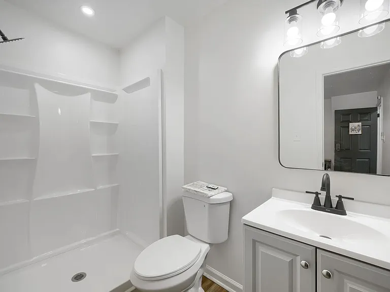Updated full bathroom with walk-in shower, vanity storage, and large mirror with overhead lighting.