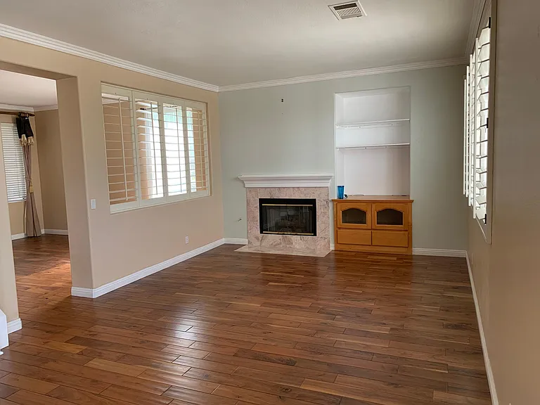 Family room next to living room with fireplace, entertainment center, window shutters.